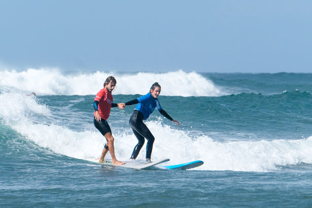 Surflehrer hilft Surfschülerin beim Wellenreiten in Fuerteventura