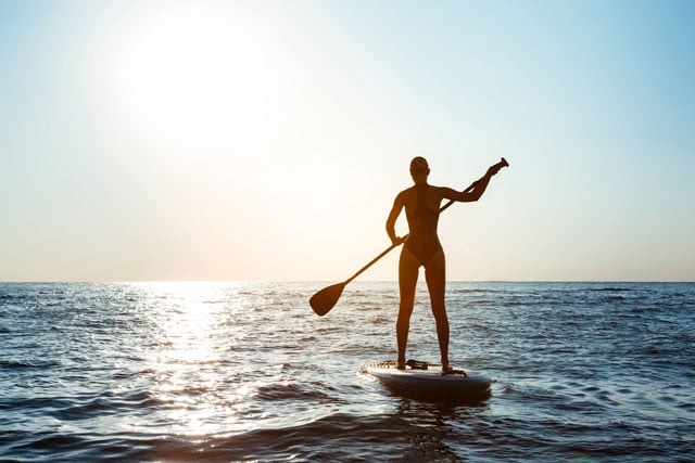 Woman moves along the water with a stand up paddle board